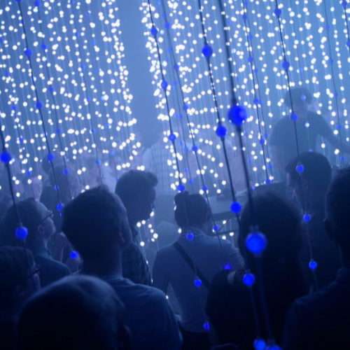 Photo of a crowd of people surrounded by strings of blue lights