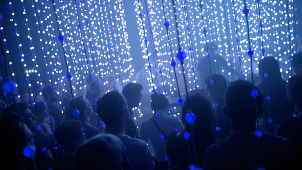 Photo of a crowd of people surrounded by strings of blue lights
