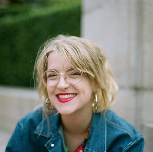 Colour portrait of a smiling young blond woman wearing spectacles and a blue denim jacket
