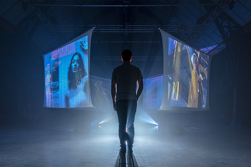 Figure standing surrounded by digital projected screens