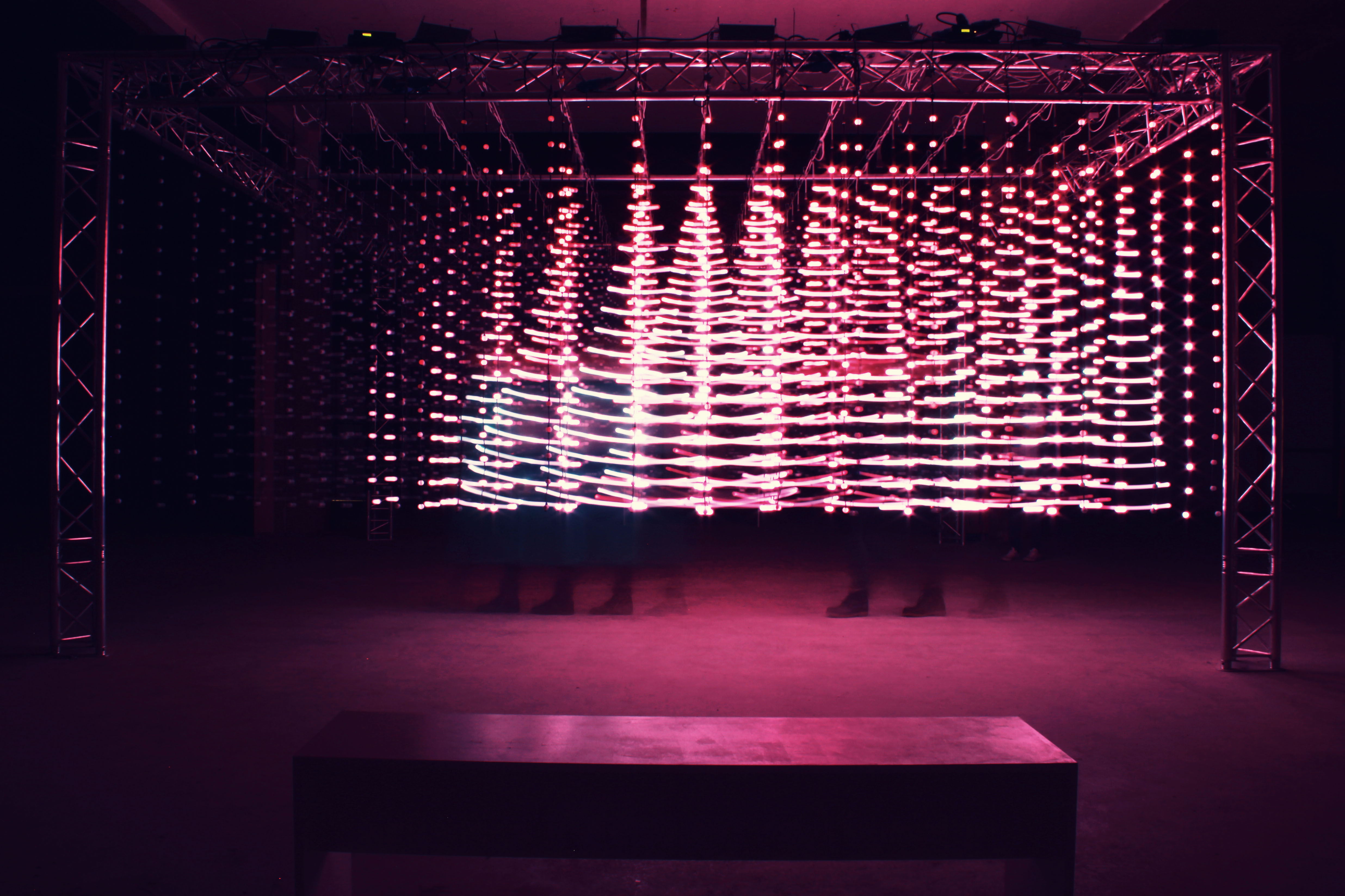 hundreds of white lights hanging from a metal frame with a red hue