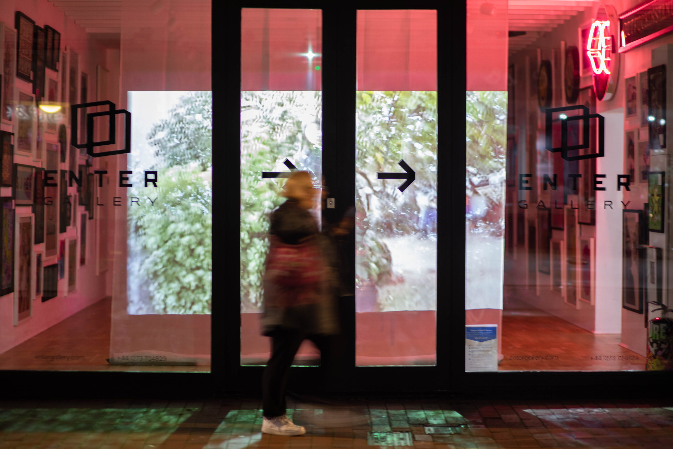digital screen with collage of photographs through a gallery window and person walking past