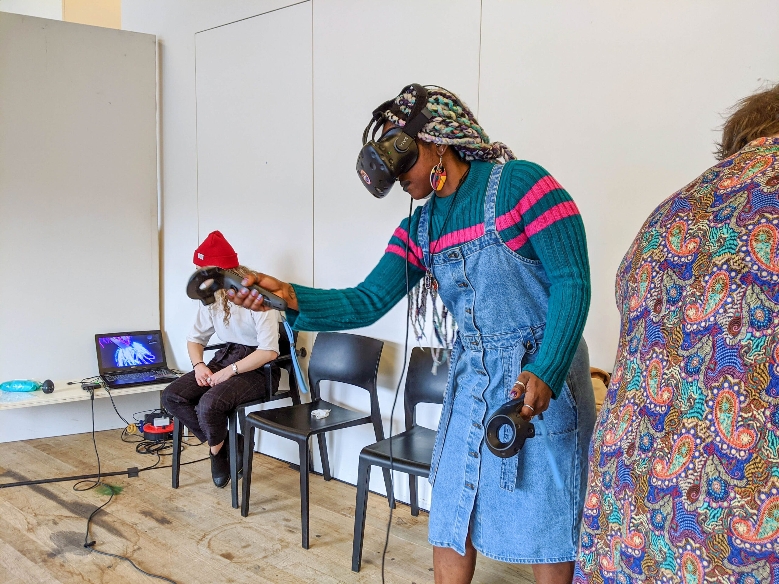 black woman with long white hair wearing a VR headset and holding a controller in a workshop space