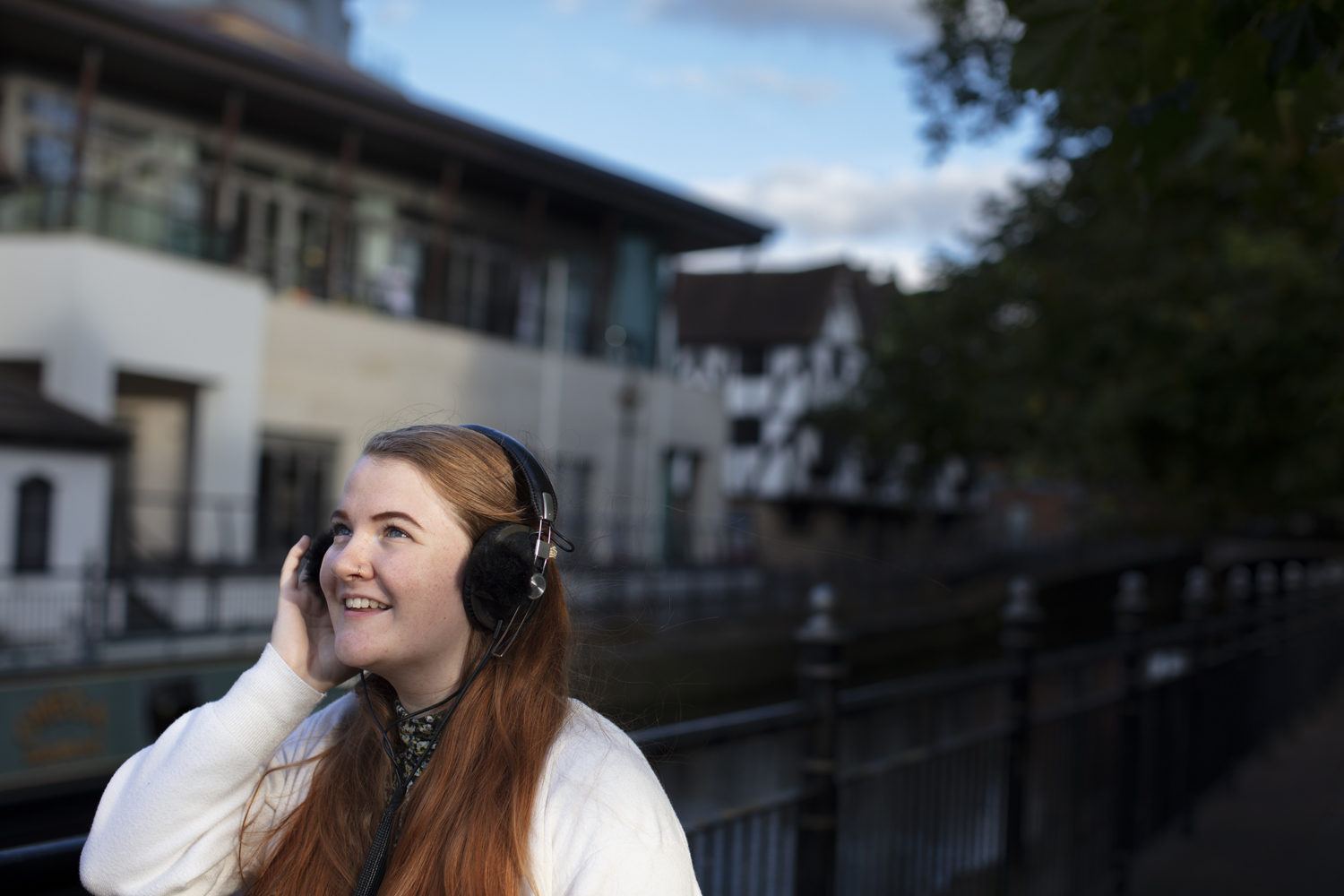 young woman with long ginger hair listening to headphones outside next to a canal