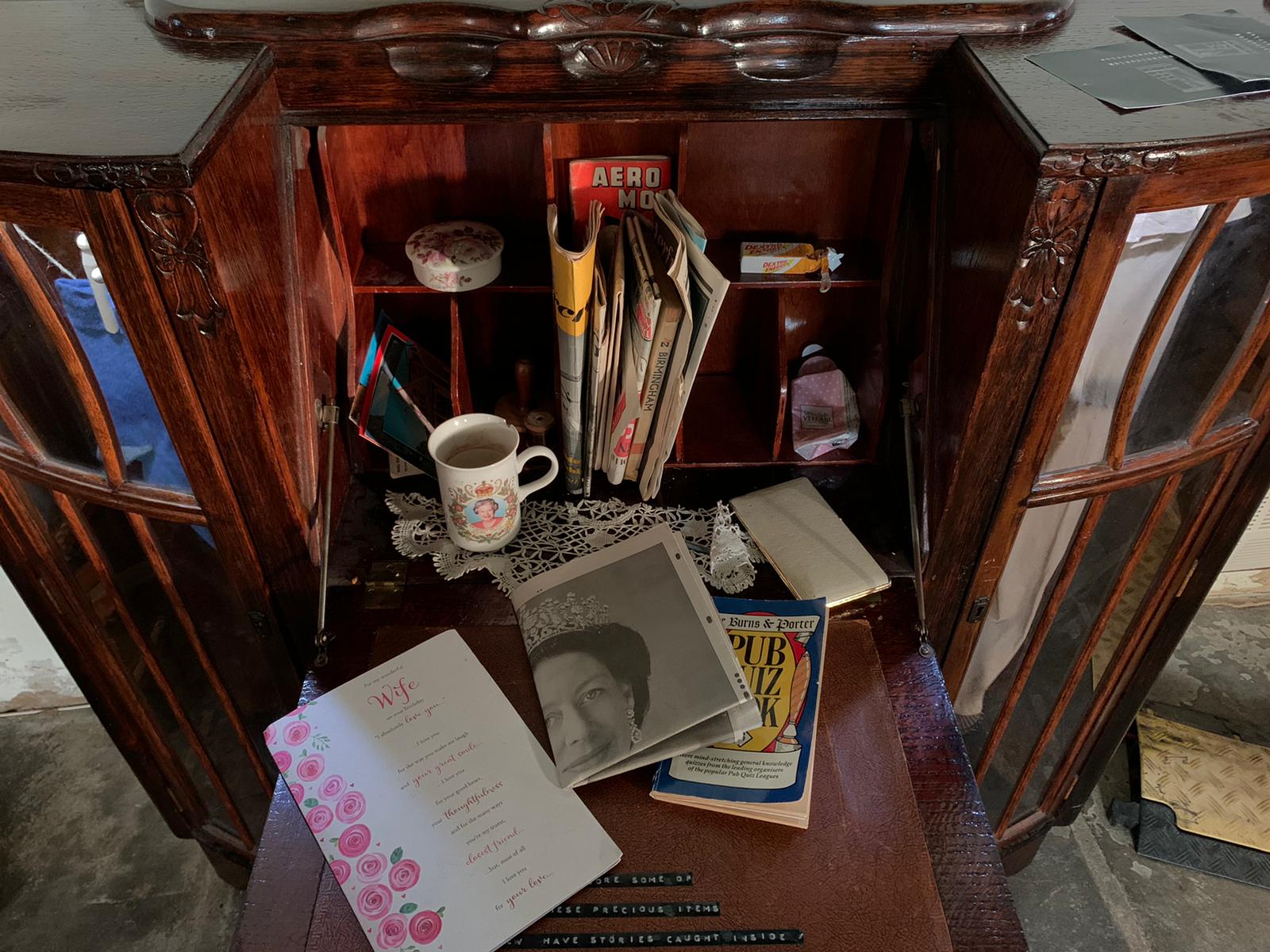 open bureau with newspapers, books and a mug on it