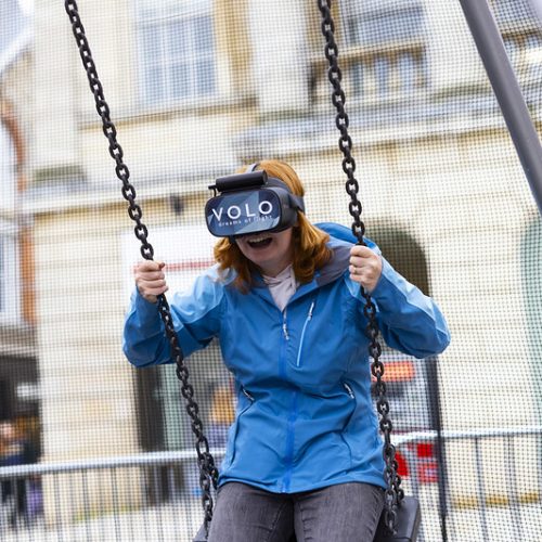 person with long red hair and blue jacket wearing a VR headset whilst swinging on a swing in Cornhill Lincoln